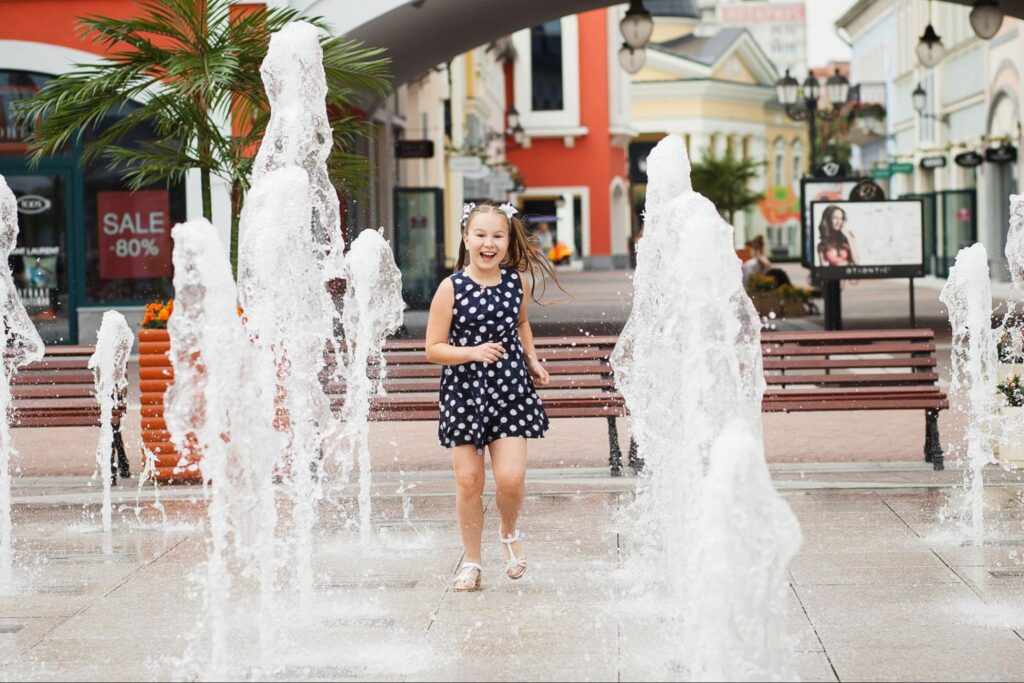 Little girl playing in an urban splash pad surrounded by modern buildings