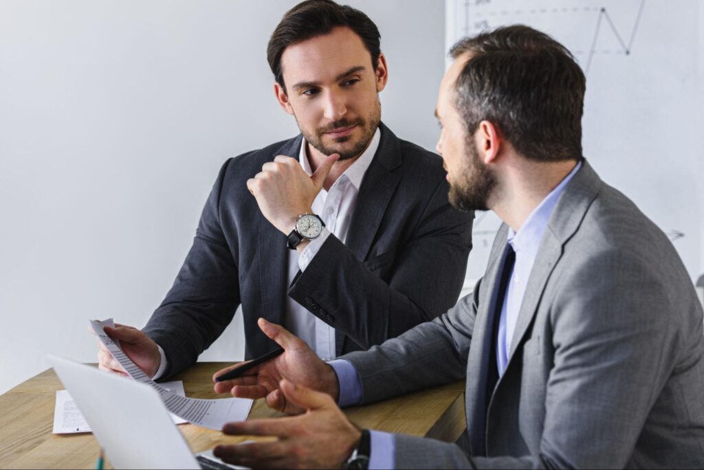 Two corporate professionals sharing a desk, one explaining key details on a document while the other listens with interest.