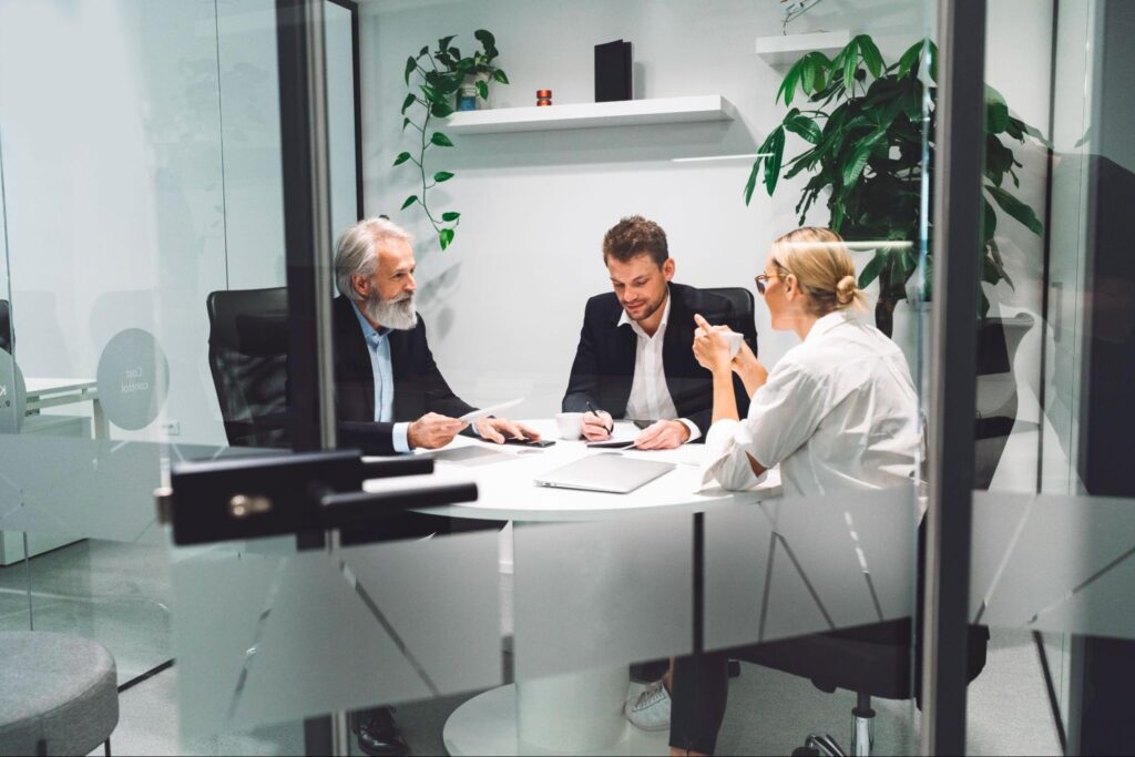 Three corporate professionals in a small office meeting room having a focused discussion.