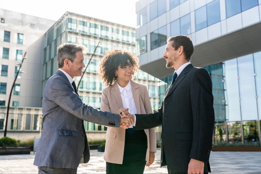 Three business professionals shaking hands, indicating a successful agreement or deal in the corporate setting.