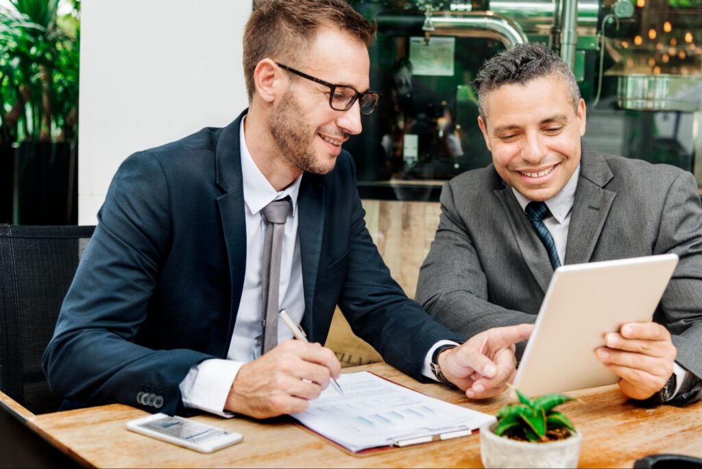 Two happy business professionals reviewing information on a tablet, one pointing and writing, signaling an agreement.